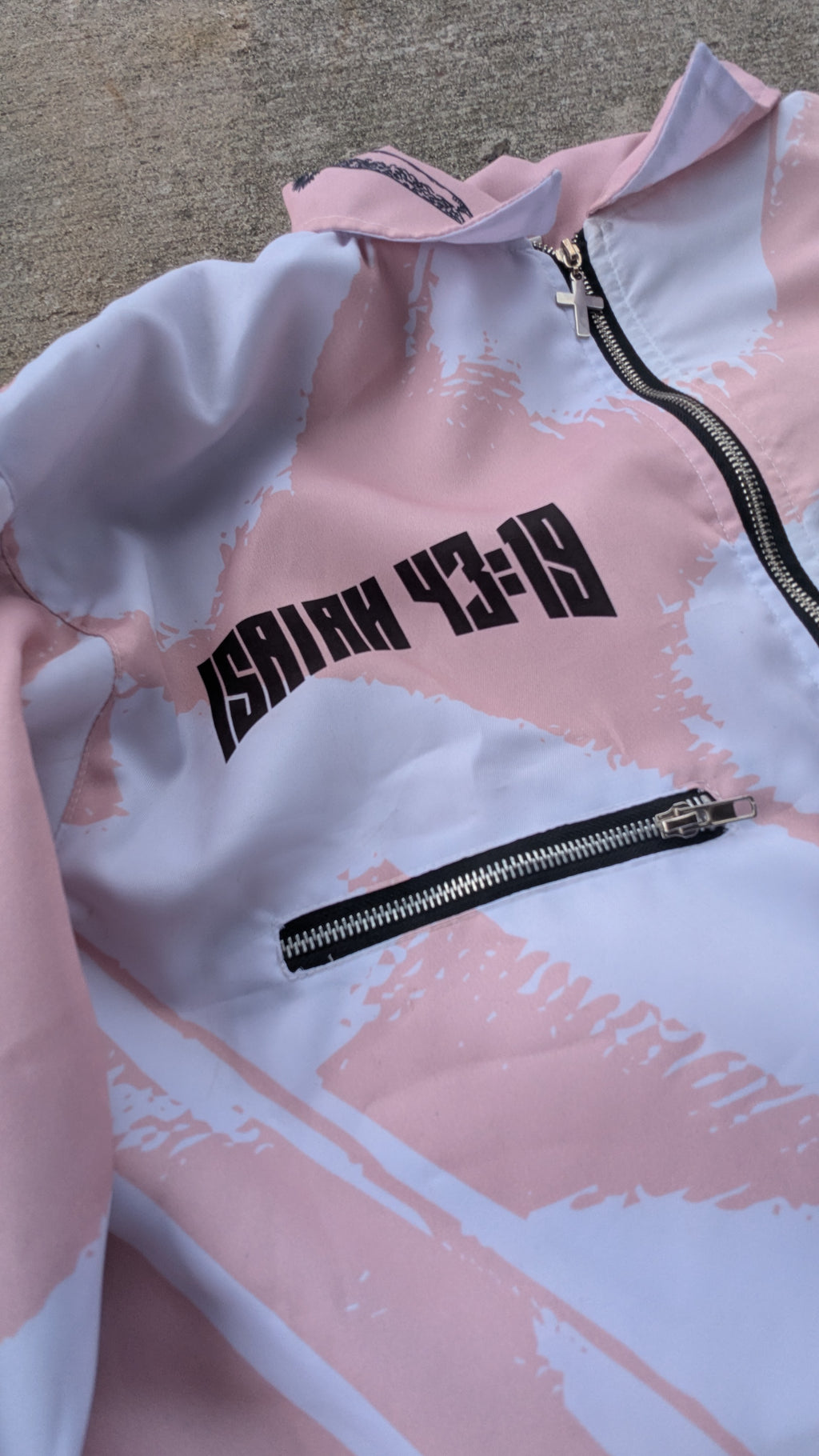 Pink and white jacket with black text and zipper on a textured surface