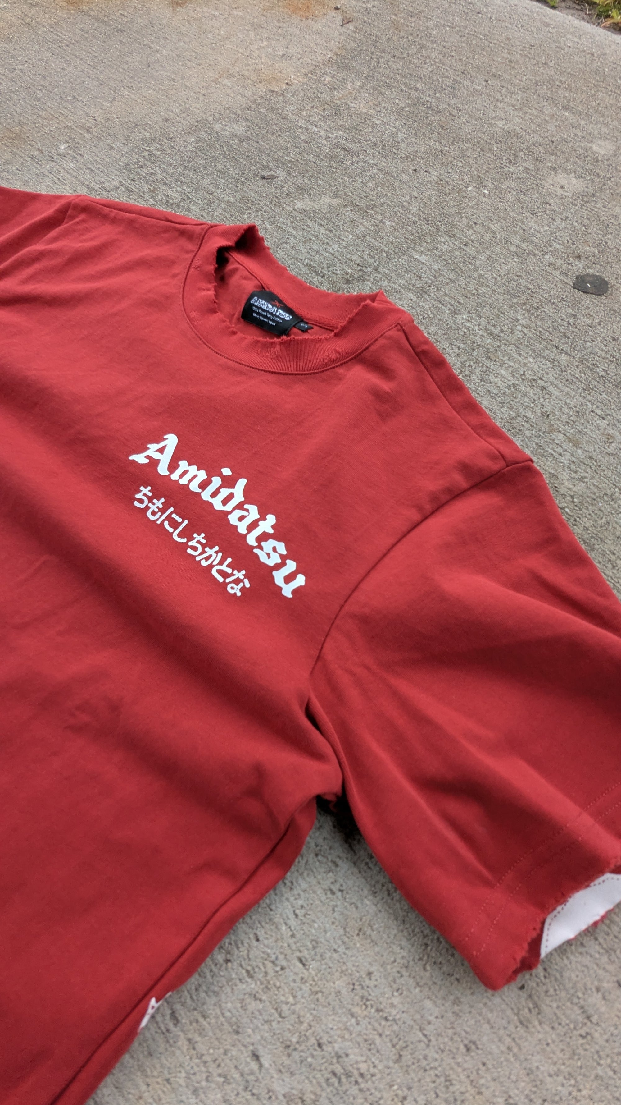 Red t-shirt with 'Amidatsu' text on a concrete surface