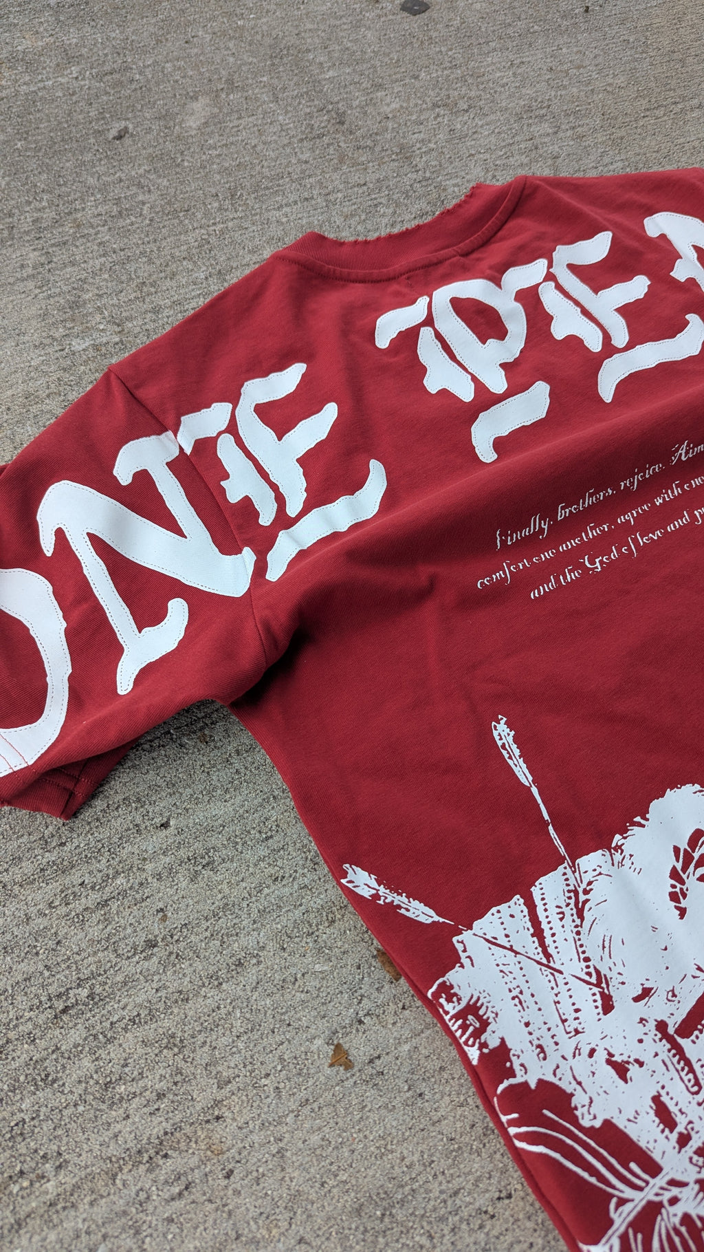 Red t-shirt with white text and graphics on a concrete surface