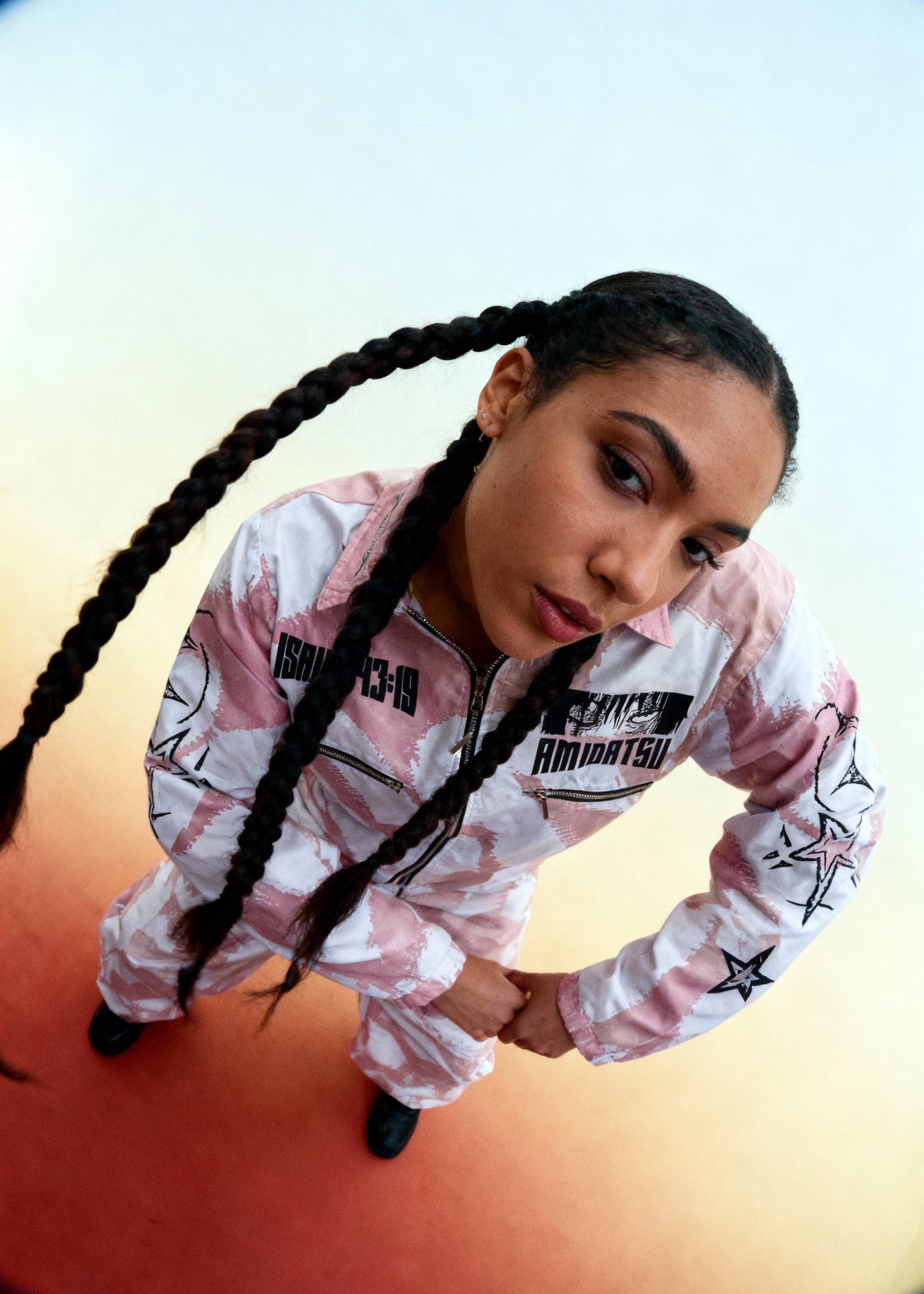 Person wearing a pink and black outfit with text, standing against a gradient background.