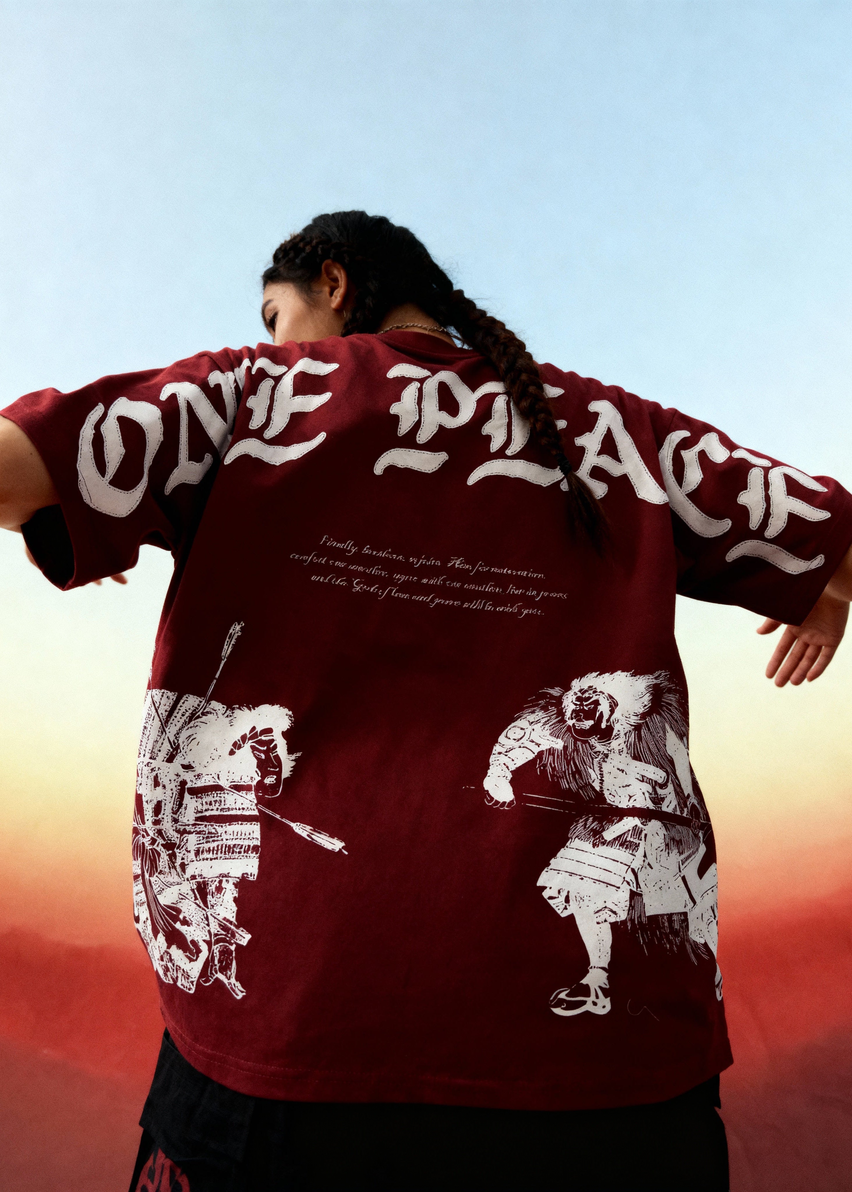 Person wearing a red 'ONE PEACE' shirt with white graphics against a sunset sky.