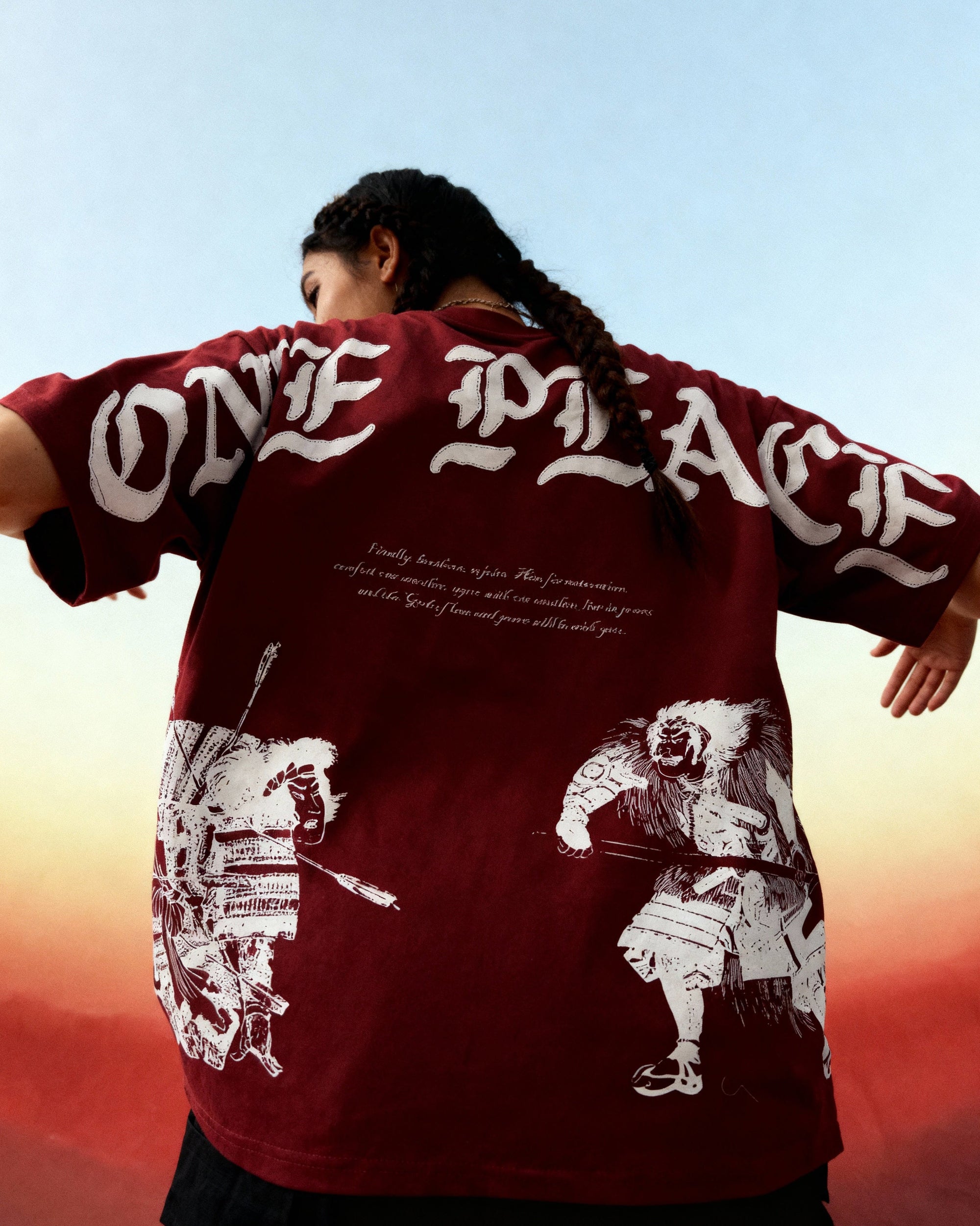 Person wearing a red 'ONE PEACE' shirt with white graphics against a sunset sky.
